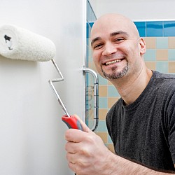 Photo of a DIY-er painting a bathroom wall by michellegibson/istockphoto.com.